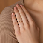 A hand with nude nails wears the Duo Vertical Baguette Ring—a delicate gold ring with two small red stones on the ring finger, making it a perfect personalized gift.