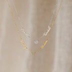 The Grace Name Heart Necklace features two layered name necklaces—one silver, one gold—each personalized in cursive and accented with a sparkling pavé heart charm.