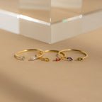 Four delicate gold rings, including the Duo Marquise Birthstone Ring, showcase marquise-cut gemstones in assorted colors and are elegantly displayed on a neutral beige surface.