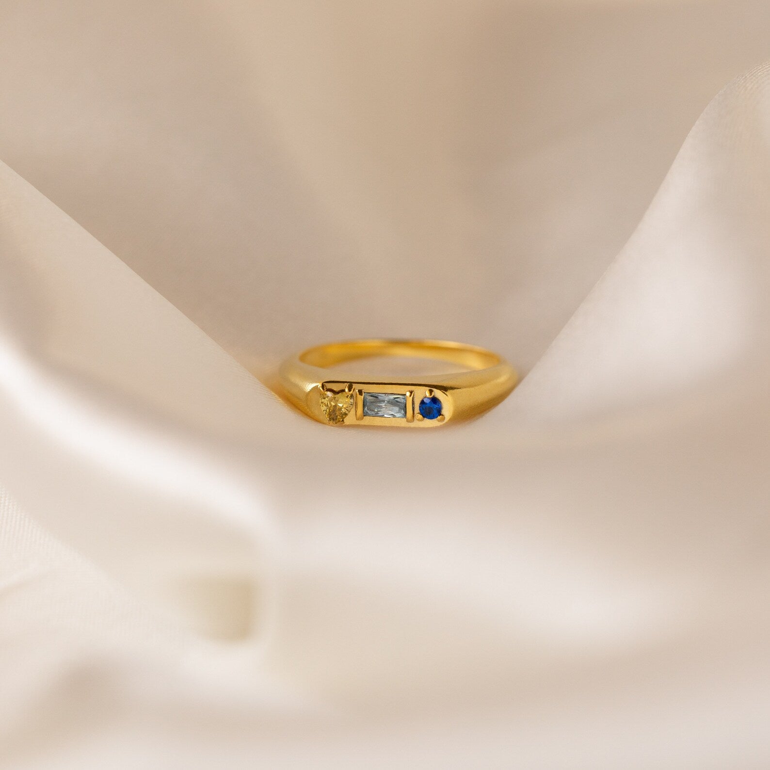 The Bold Birthstone Signet Ring in Rose Gold showcases three customizable gemstones, displayed on soft white fabric.