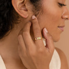 A woman touches her face, wearing the Bold Birthstone Signet Ring adorned with colorful gemstones on her finger.