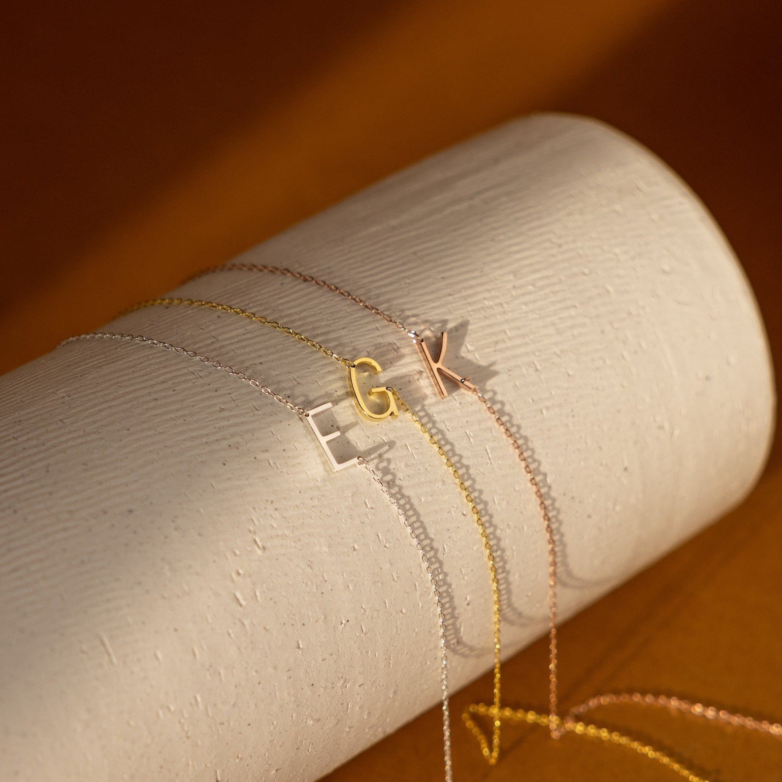The Mini Sideways Initial Necklace comes in gold, silver, or rose gold with a textured cylinder and an E, G, or K pendant—an elegant personalized gift.