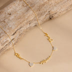 Grace Name Heart Necklace features a gold chain with personalized cursive name and Mom charms, plus two small heart pendants—an elegant custom necklace for any occasion.