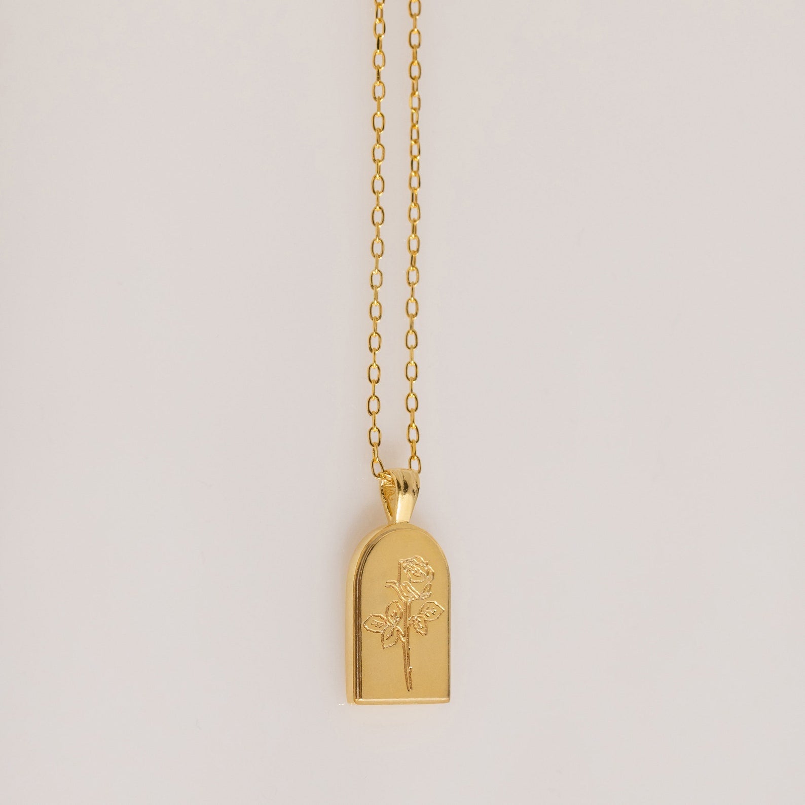 The Birth Flower Arch Necklace features a rectangular pendant with a rose engraving, displayed on a simple background—a beautiful personalized jewelry piece to enhance any outfit.