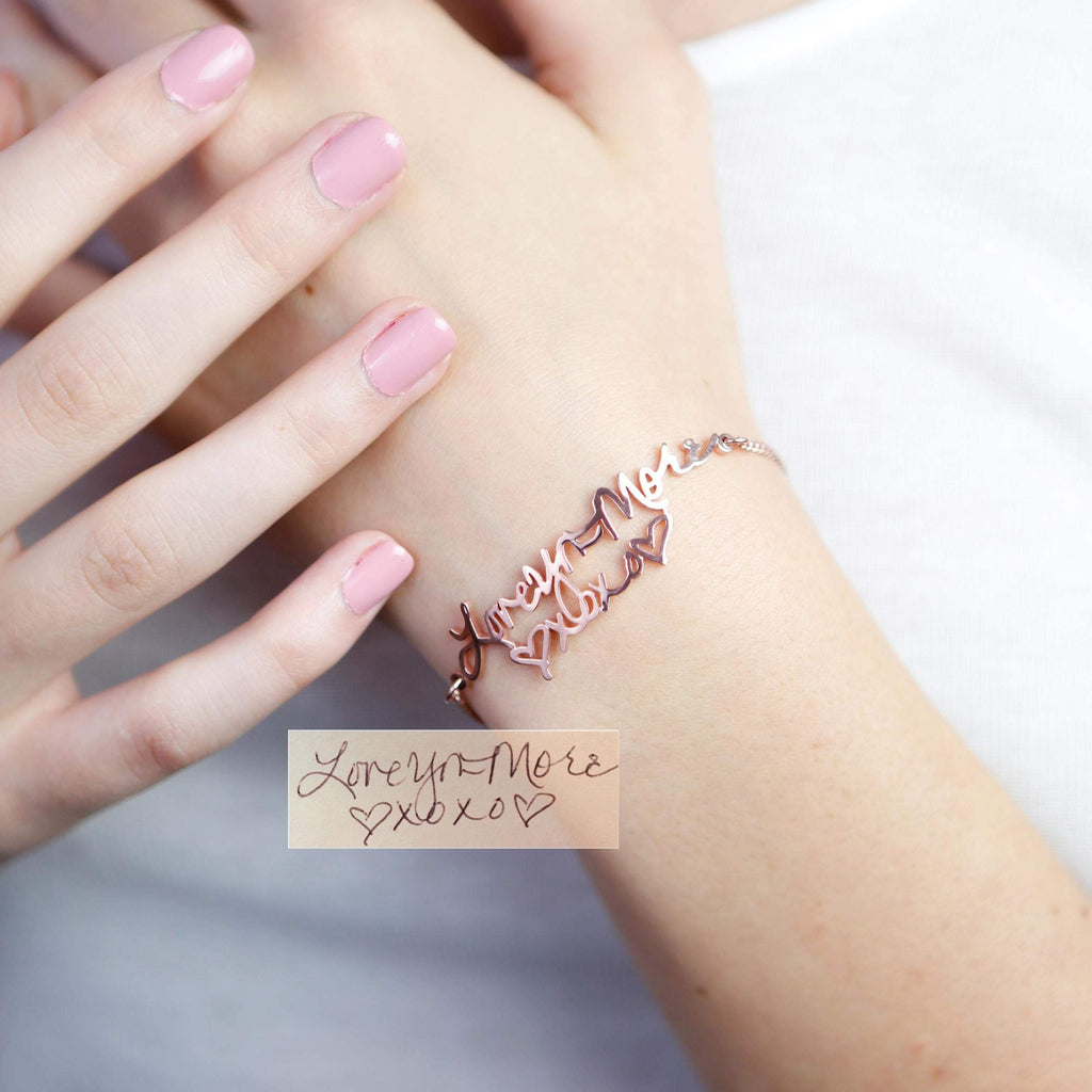 Close-up of a hand wearing the Handwriting Bracelet in rose gold, engraved with "Love You More" and heart shapes—an ideal personalized piece for everyday wear.