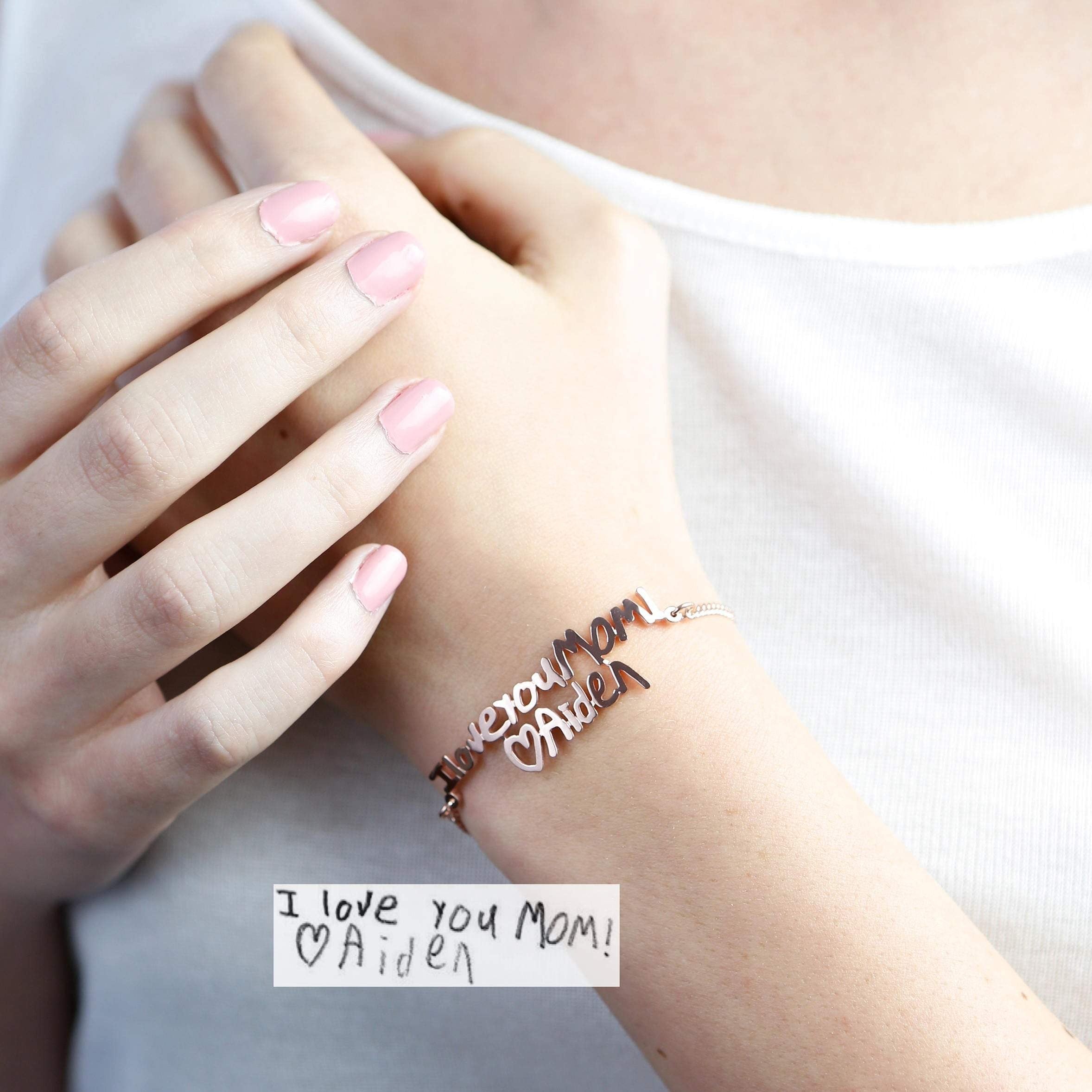 A hand wears a Handwriting Bracelet personalized with "I love you Mom! ♡Aiden," matching the handwritten note below.