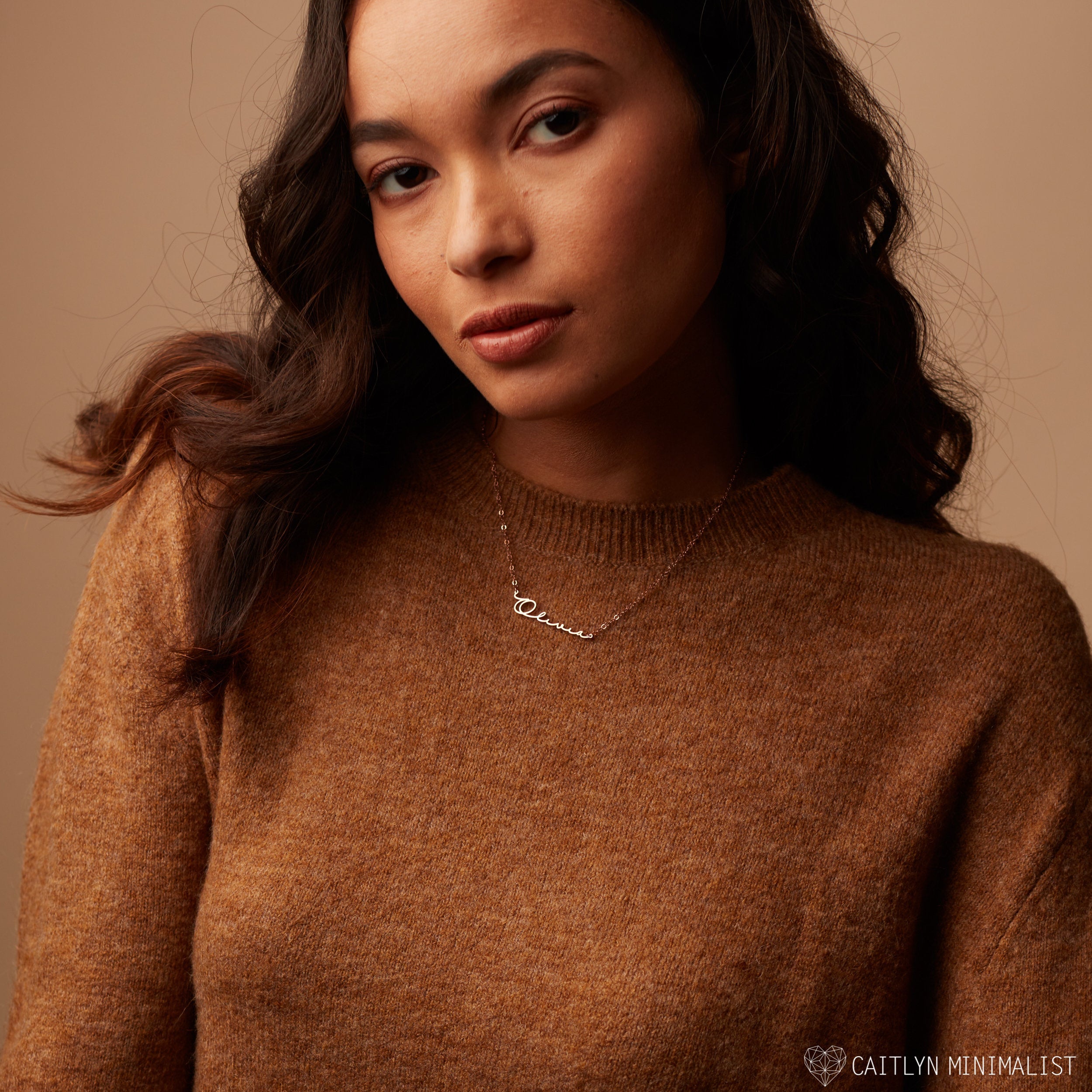 Woman wearing a brown sweater and the Minimal Name Necklace, posing against a neutral background.