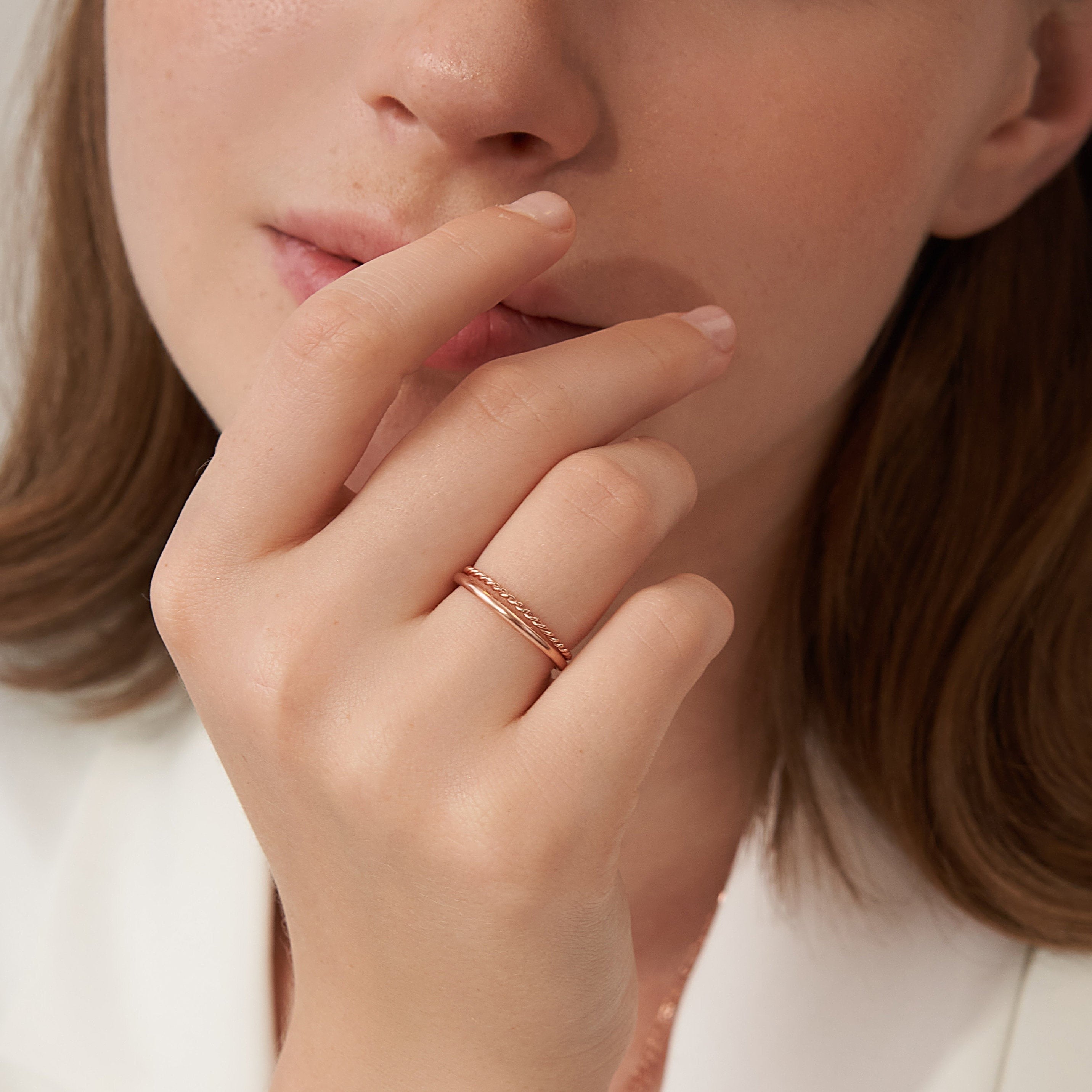 A woman touches her lips while wearing a delicate ring from the Minimalist Stacking Ring Set—perfect for stacking or adding to your favorite minimalist look.