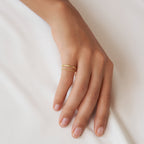 A hand wearing a gold ring from the Minimalist Stacking Ring Set rests on a white fabric surface.