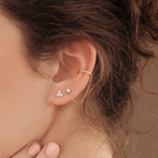 Close-up of a woman's ear adorned with Pave Chain Ear Cuffs in gold, paired with two diamond stud earrings and featuring a delicate chain accent.