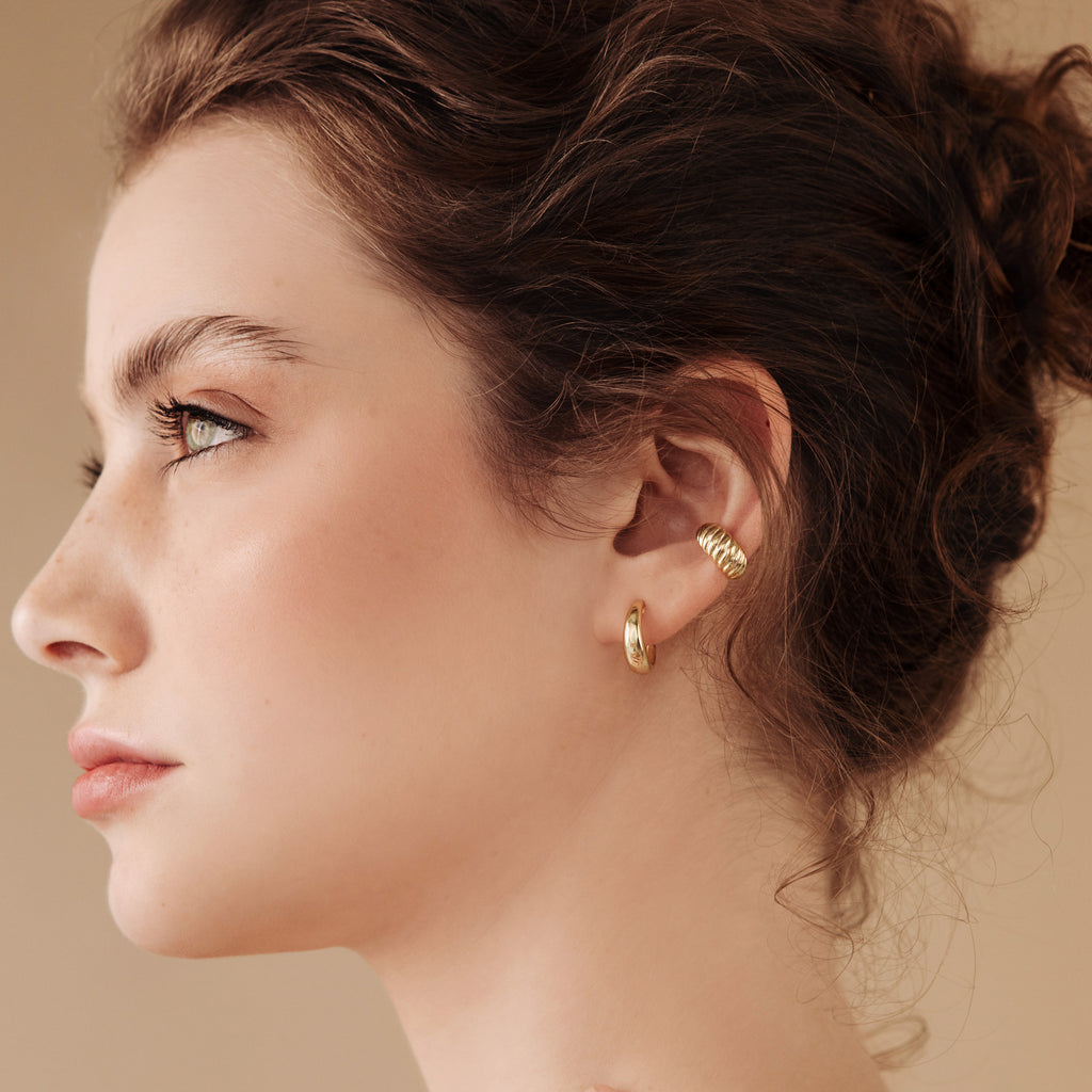 A woman with curly brown hair wears Dome Hoops and gazes to the left against a beige background.