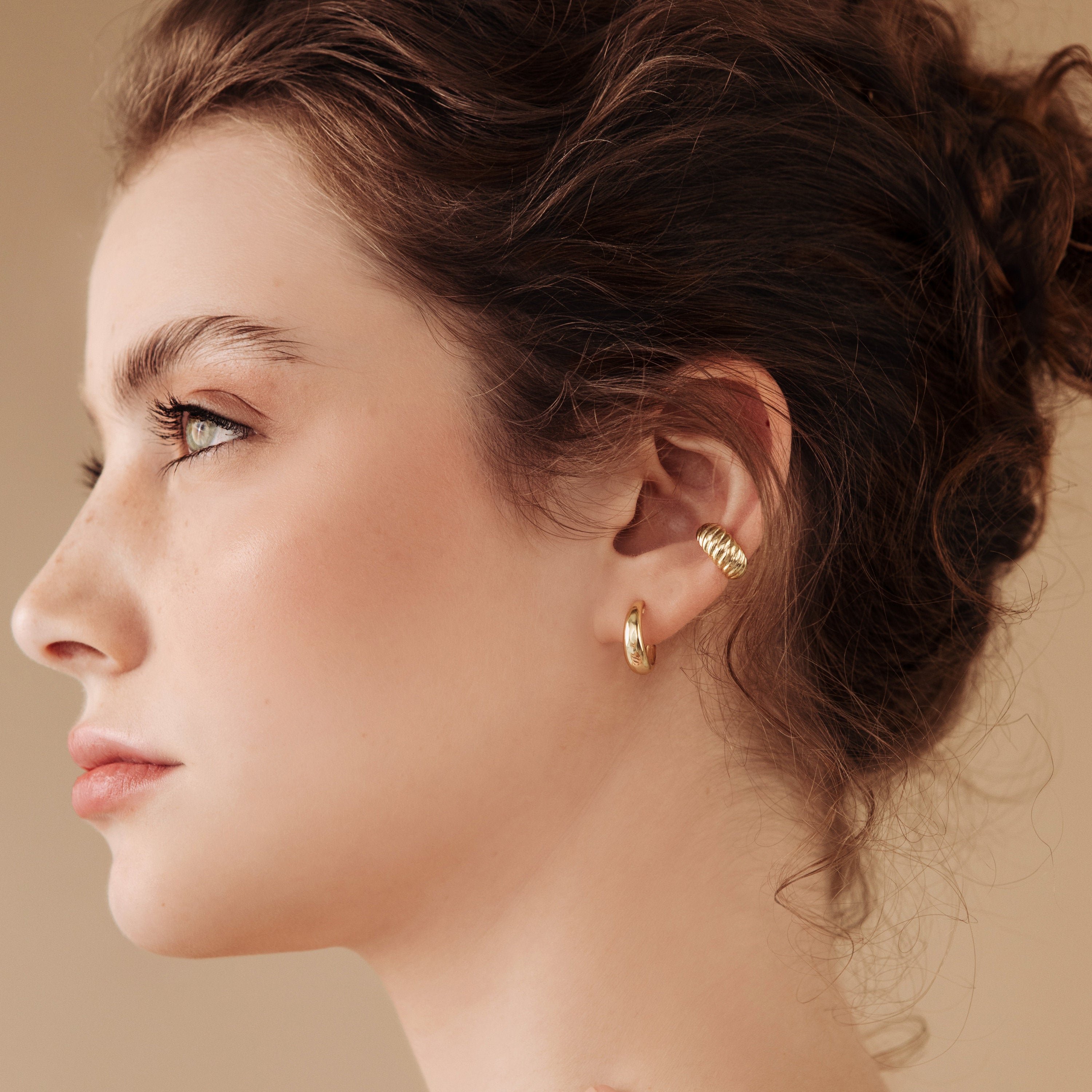 A woman with curly brown hair wears Dome Hoops and gazes to the left against a beige background.