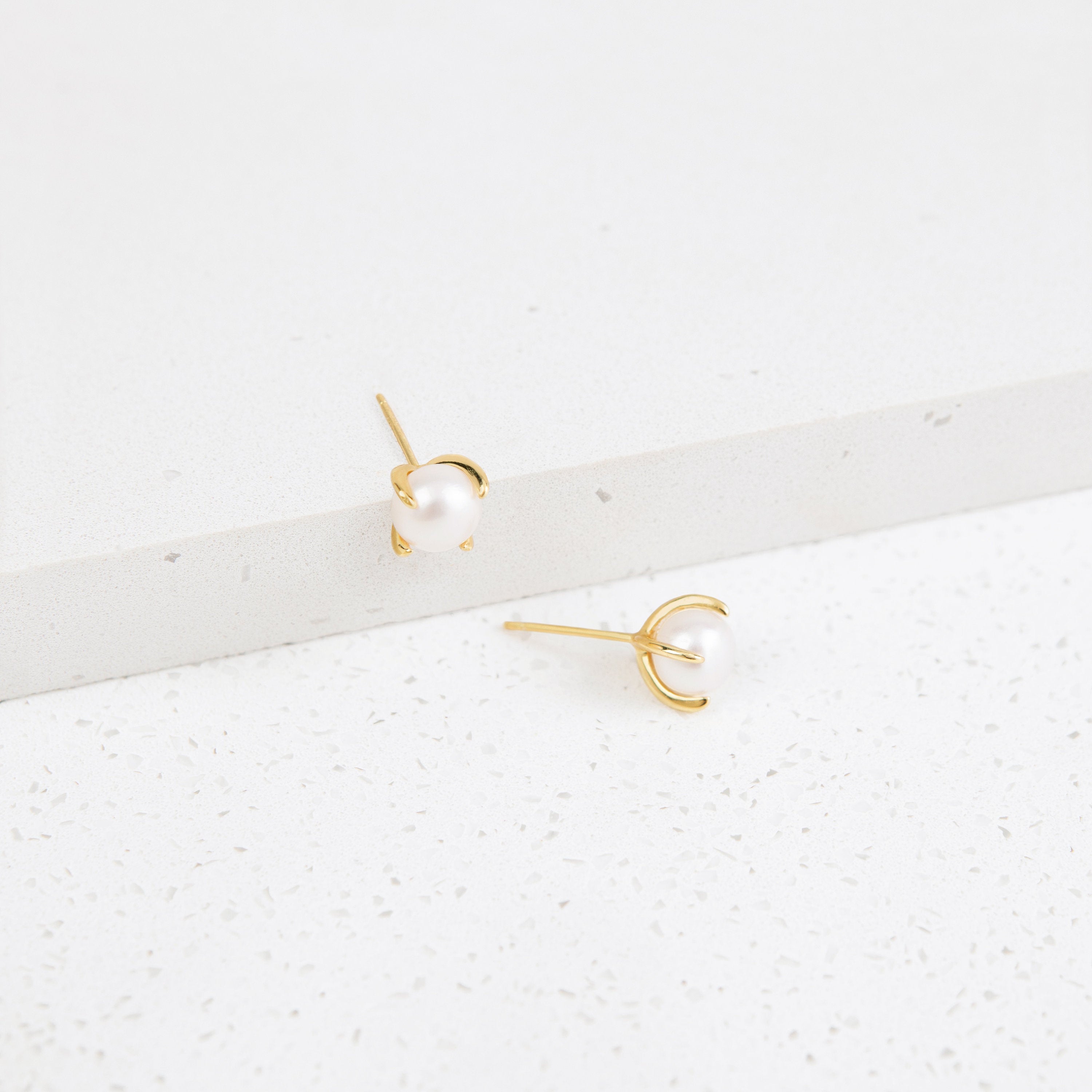 Zoe Pearl Studs shown on a white, textured surface blend contemporary style with timeless elegance, making them the perfect pearl earrings for any occasion.