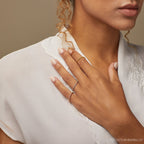 A woman in a white blouse displays her hand adorned with three delicate rings, including the Lea Twisted Ring and polished bands on her fingers.