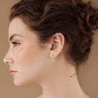 Profile of a woman with curly brown hair, wearing gold Bar Ear Cuffs and pave bar earrings, on a beige background.