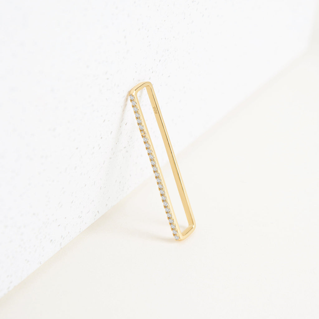A pair of Bar Ear Cuffs, rectangular in shape with small embedded diamonds, reminiscent of pave jewelry, are leaning against a white textured surface.