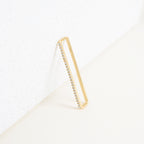 A pair of Bar Ear Cuffs, rectangular in shape with small embedded diamonds, reminiscent of pave jewelry, are leaning against a white textured surface.