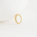 The Twisted Dome Ring stands upright on a white surface, its elegant gold curves highlighted against a minimal, clean background.