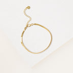 The Essential Bracelet Chains feature a delicate gold chain with polished finishes and an adjustable clasp, shown on a white textured surface.