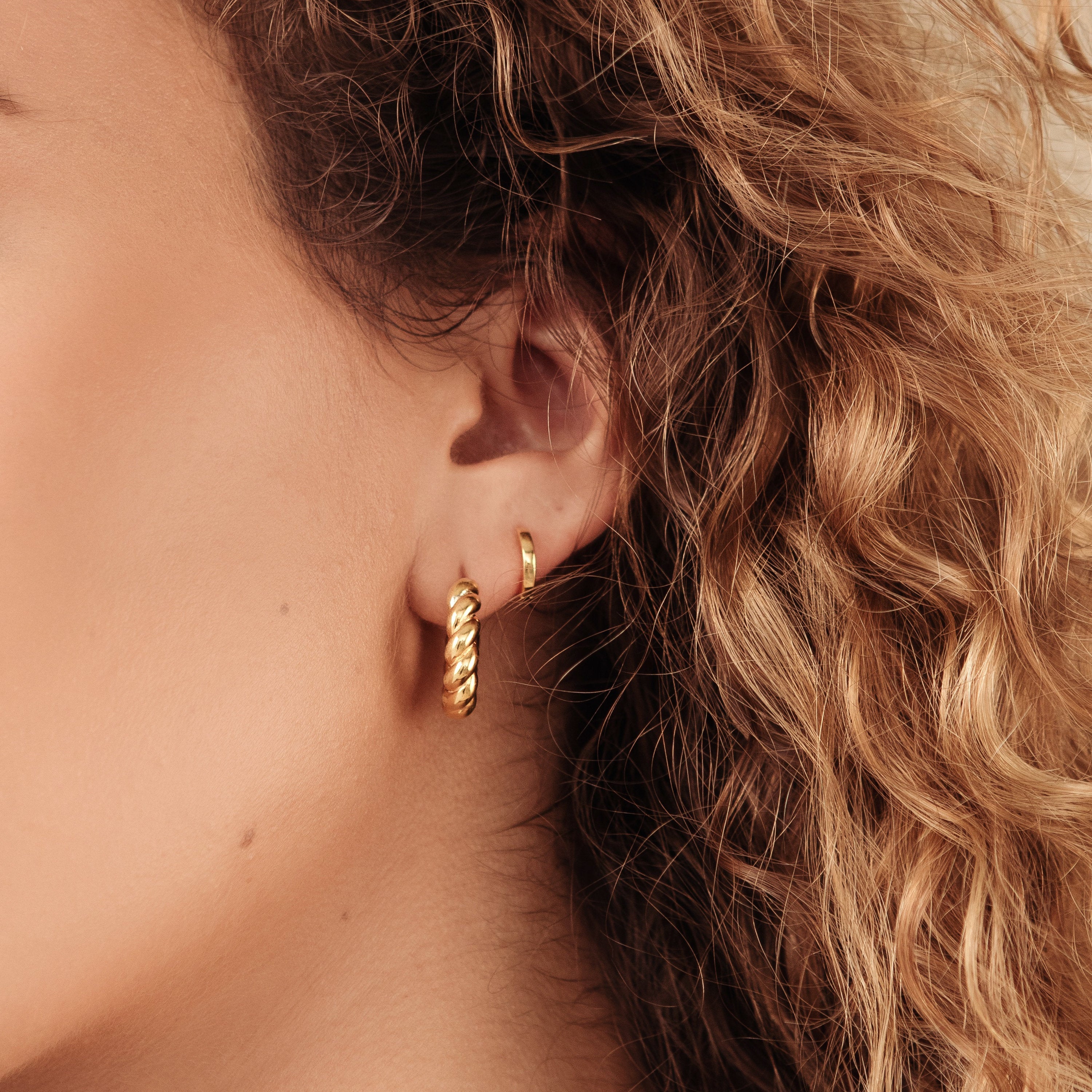 Close-up of a woman's ear with two Editor Huggies and curly blonde hair, highlighting their minimal aesthetic and classic jewelry style.