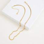 A close-up view of a gold herringbone necklace resting on a terrazzo display block.