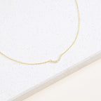 The Lucia Pave Necklace is a delicate gold chain with a small crescent charm pendant adorned with tiny crystals, beautifully displayed on a white surface.