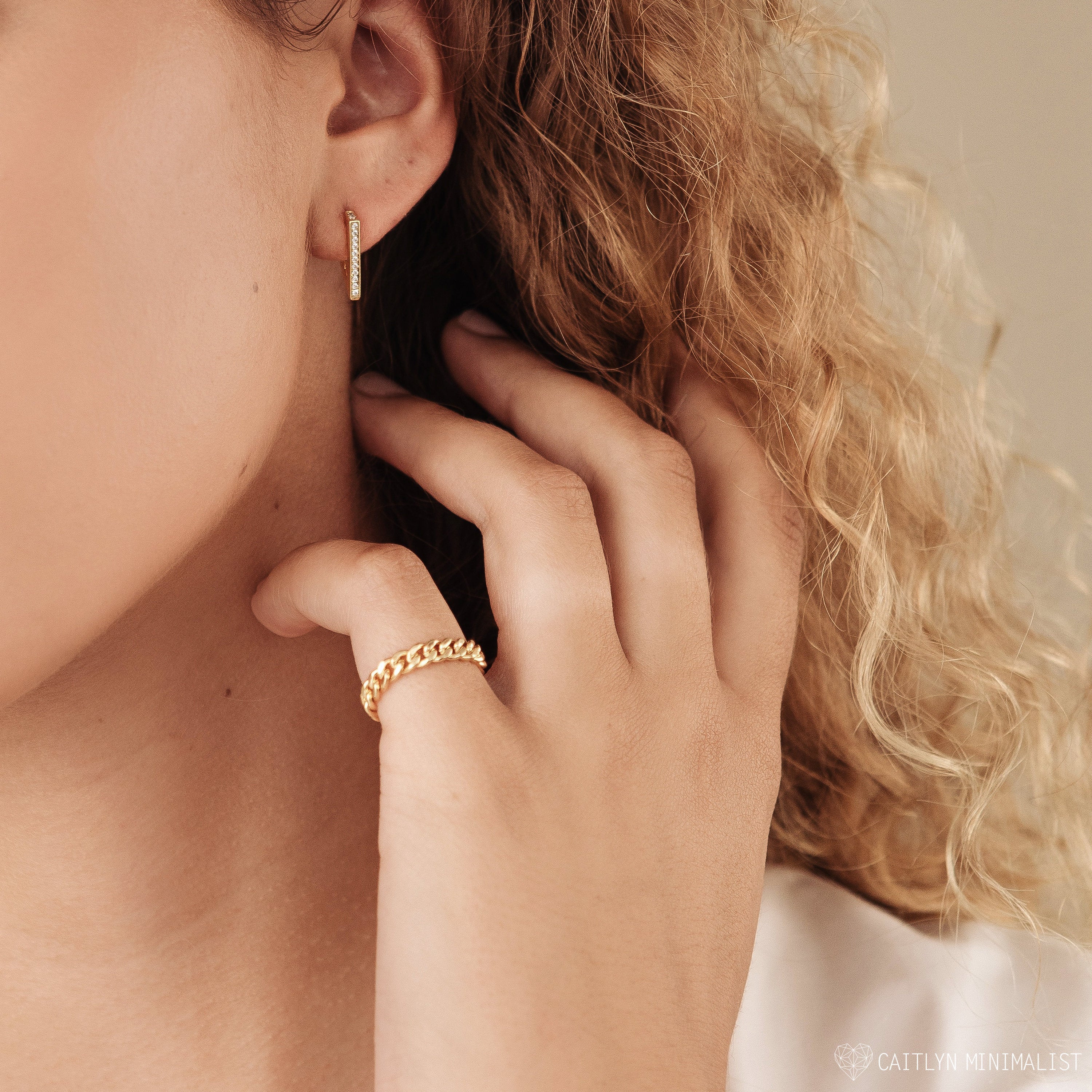 Close-up of a woman's hand touching her face, wearing the Curb Chain Ring, a gold piece perfect for adding subtle goth glam jewelry vibes.