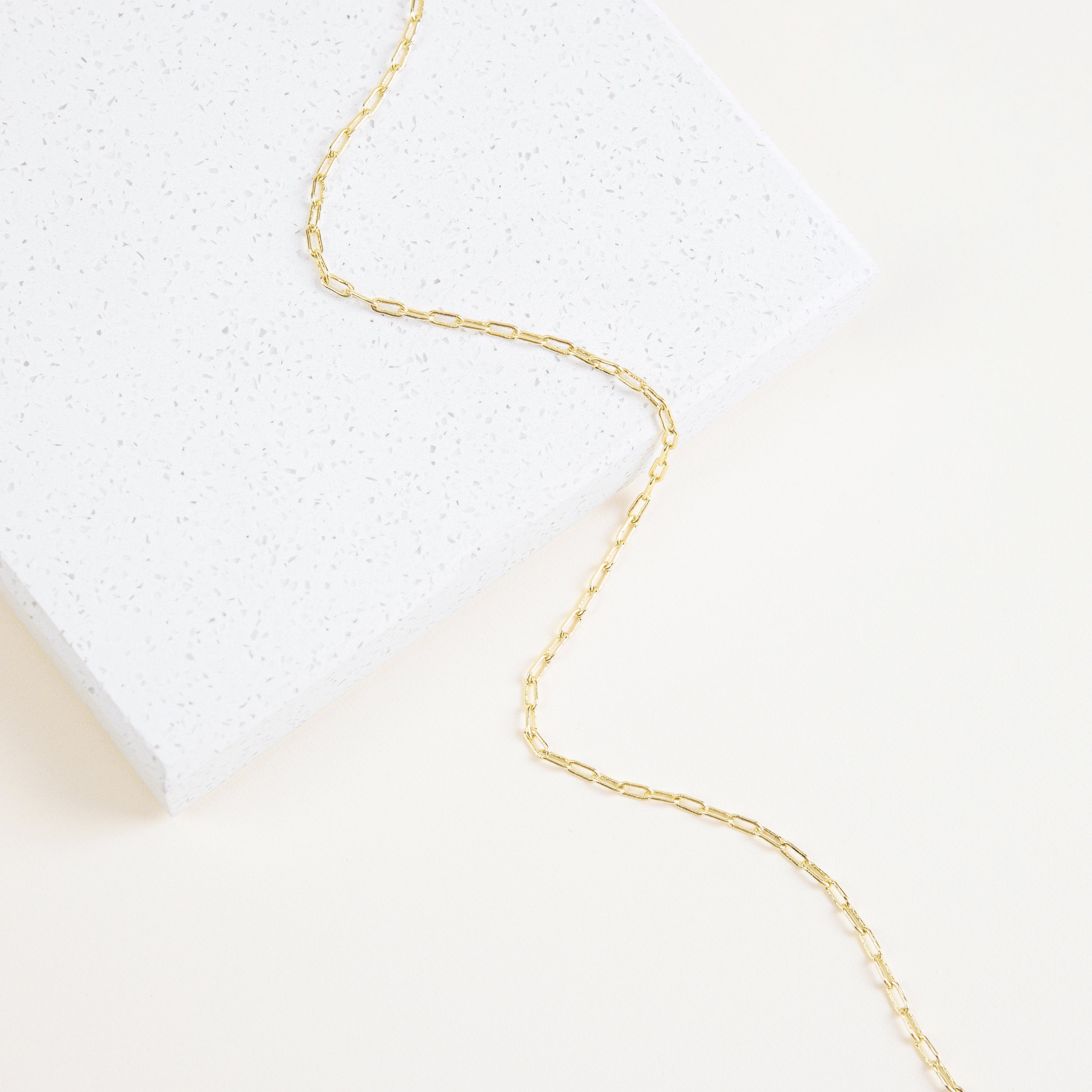 The Dainty Link Chain Necklace in Rose Gold features delicate rectangular links draped over a white, speckled surface—perfect for layering with your favorite necklaces.