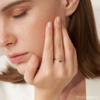 A woman touches her face, wearing the Initial Heart Wrap Ring—this customizable rose gold ring features initials, creating a unique and personal symbol of love on her finger.