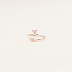 The Initial Heart Wrap Ring features a gold band with a letter K and a heart on opposite ends—an elegant symbol of love. Personalize it with any initial for a unique touch, beautifully displayed against a plain backdrop.