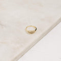 The Pave Signet Ring, adorned with a cluster of small diamonds, rests on a light marble surface, offering a modern-luxe statement accessory.