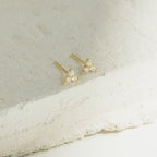 Mini Lily Studs: Dainty gold earrings each featuring three clear gemstones, ideal for everyday wear or stacking in cartilage piercings. Shown on a textured white stone surface.