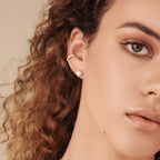 Close-up of a woman's face with curly hair, a gold hoop earring, and glimmering Mia Pave Cuffs diamond huggie earrings.