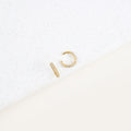 The Mia Pave Cuffs, gold hoop earrings adorned with small clear stones, sparkle beautifully on a white speckled surface.