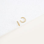 The Mia Pave Cuffs, gold hoop earrings adorned with small clear stones, sparkle beautifully on a white speckled surface.