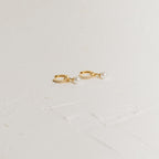 Mae Huggies: Gold hoop earrings accented with pearls and small crystals are displayed on a textured white surface—perfect for those who love timeless pearl huggies.