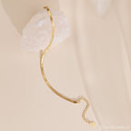 A Herringbone Anklet draped over a white crystal on a beige surface, highlighting the polished ankle jewelry's effortless elegance.