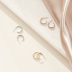 Three pairs of Chloe Hoops in silver, gold, and rose gold rest on marble and satin—polished bands that are ideal for everyday wear.