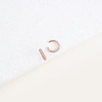 The Mia Pave Cuffs are rose gold earrings with small clear stones, sparkling beautifully on a white speckled surface.