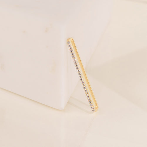 Bar Ear Cuffs with small gemstones rest against a white marble block on a cream background.