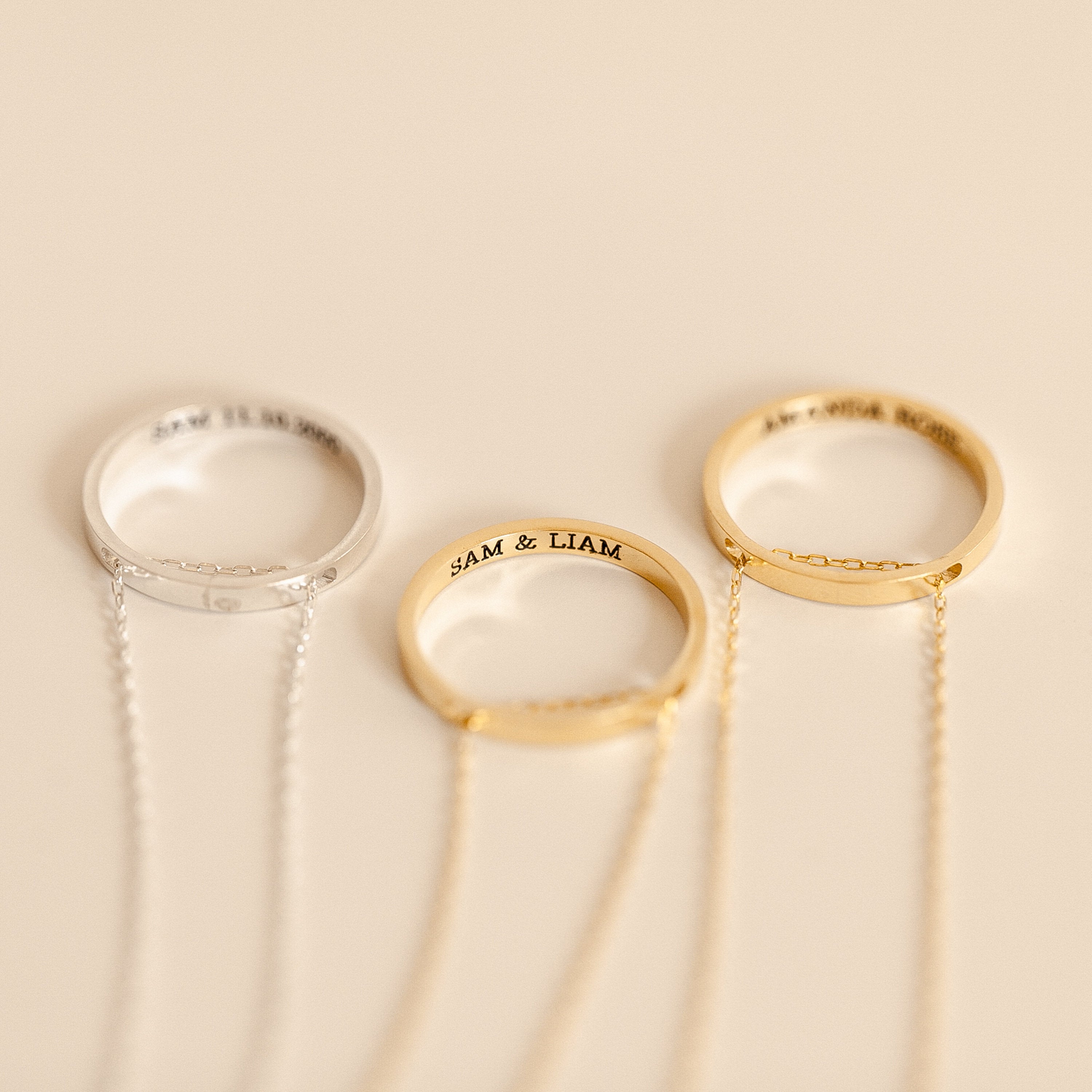The Inner Circle Necklace in Rose Gold features three engraved rings with delicate chains—two gold, one silver—evoking amulet style, all set against a light beige background.
