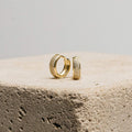 Pave Diamond Huggies rest on a textured stone block against a plain background—an elegant jewelry box essential, featuring sparkling diamond-encrusted hoops.