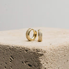 Pave Diamond Huggies rest on a textured stone block against a plain background—an elegant jewelry box essential, featuring sparkling diamond-encrusted hoops.
