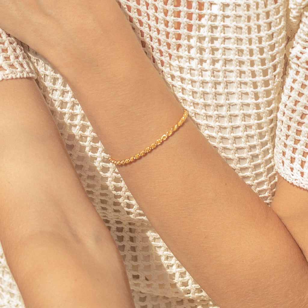 A person wearing the Rope Chain Bracelet styled with a white textured, netted top.