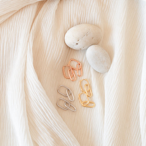 The Amanda Link Earrings in 18K Gold, with a minimalist design, are displayed on cream-colored textured fabric.