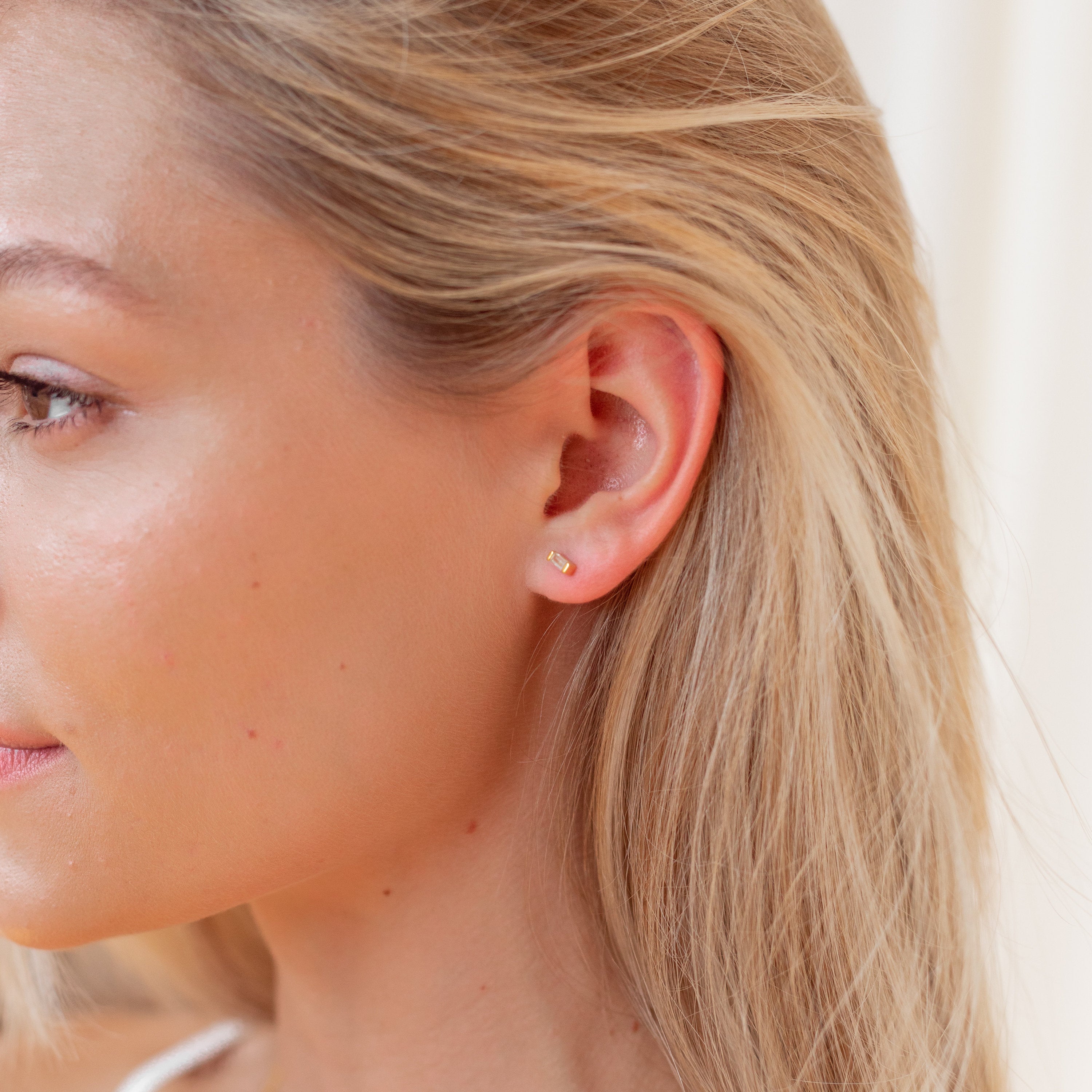 A woman with blonde hair wears Baguette Diamond Studs in her left ear.