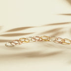 Nine Skinny Zodiac Rings in gold and silver are neatly arranged on a beige surface, with soft shadows in the background.