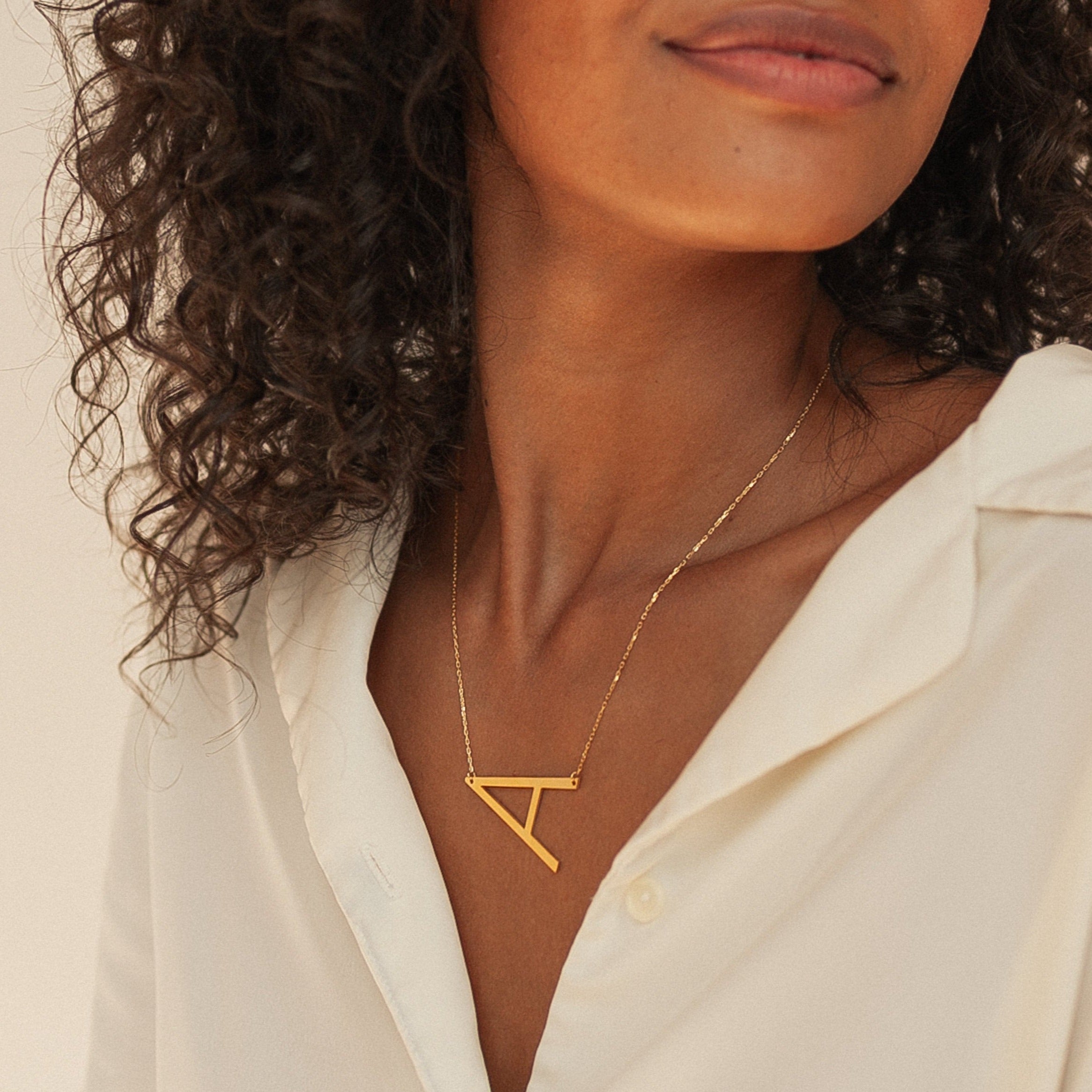 Woman wearing a white shirt and the Large Sideways Initial Necklace featuring a bold gold letter pendant, making it a true statement essential.