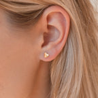 Close-up of an ear wearing Classic Heart Studs, small gold heart earrings with blonde hair partially visible—ideal for those who love cute, dainty jewelry.
