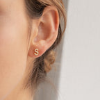 Close-up of a woman's ear wearing Pave Letter Studs, gold earrings shaped like the letter S, for a personalized minimalist look.